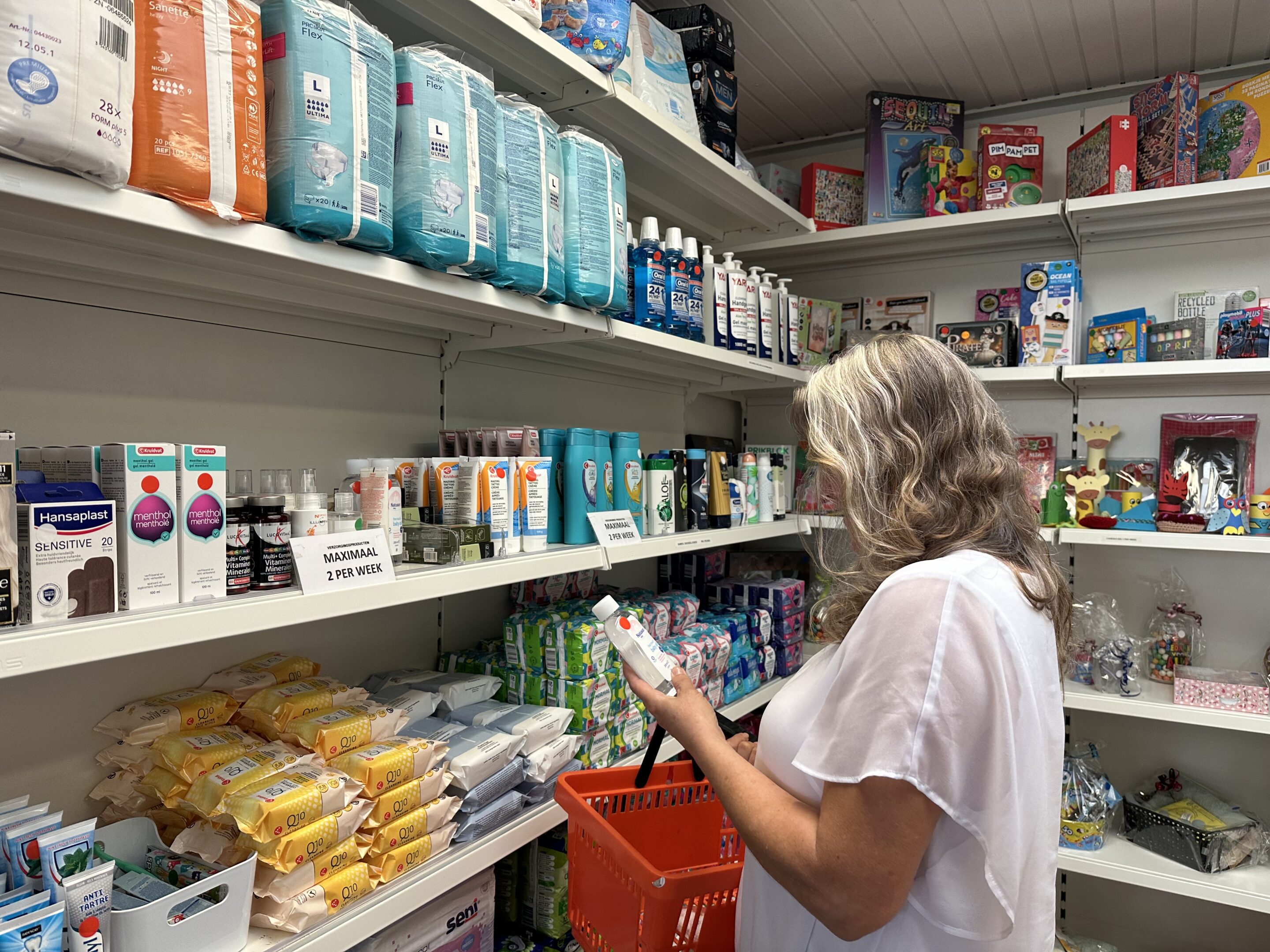 image00010 Vrouw staat in Weggeefhoek en kan daar gratis verzorgingsproducten uitkiezen. Ze heeft shampoo in haar handen.